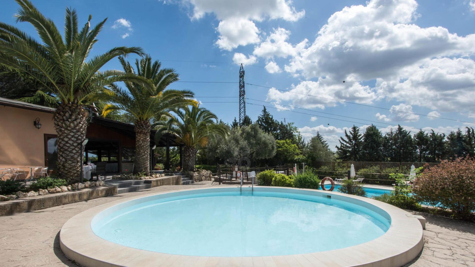 Runder Pool mit Palmen, Außensitzplätzen und schönem Himmel.