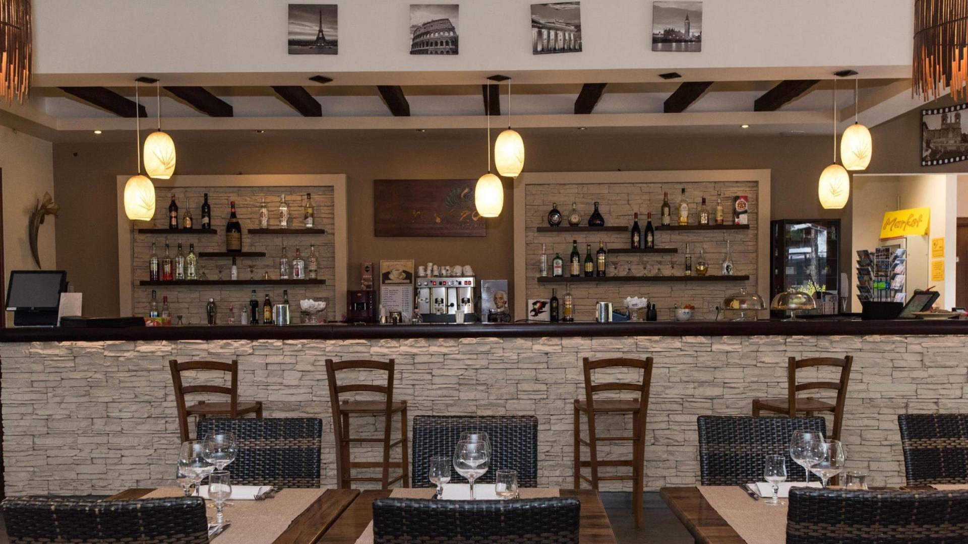 Cozy restaurant bar with wooden decor, shelves of bottles, and elegant table settings.