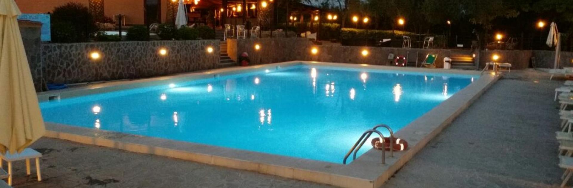 Belle piscine au crépuscule avec des lumières et des palmiers en arrière-plan.