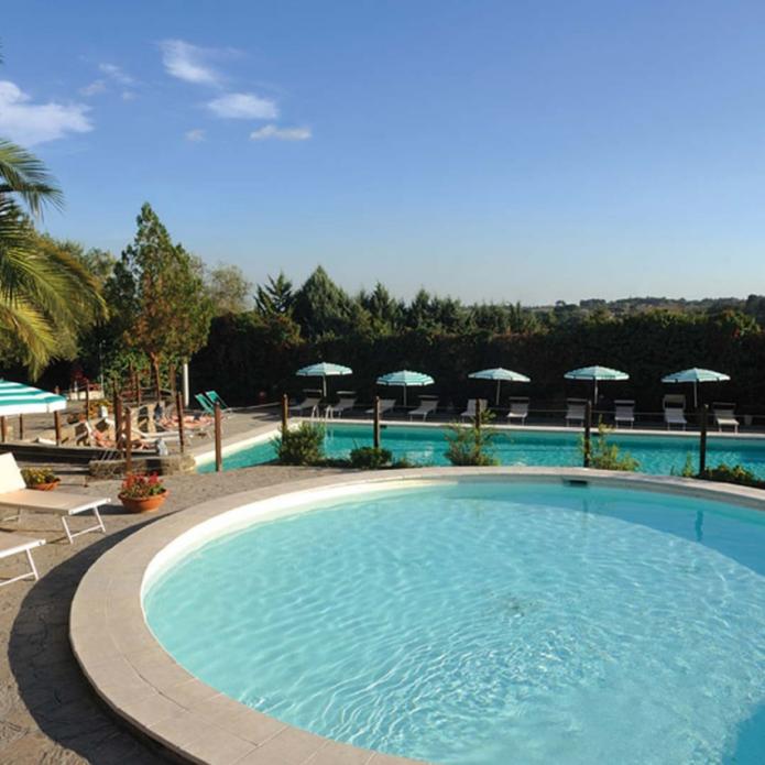 Beautiful outdoor pool area with sun loungers and umbrellas, surrounded by lush greenery.